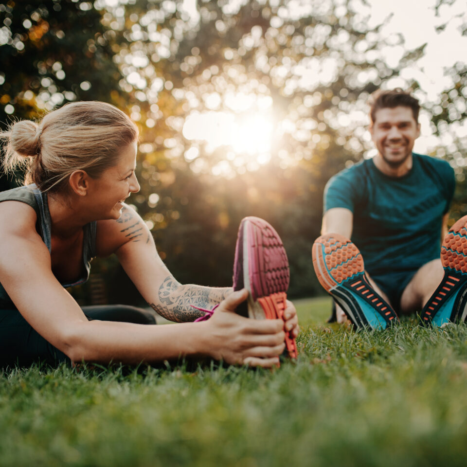 Fitness couple stretching outdoors in park. Young man and woman exercising together in morning.