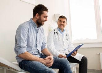 medicine, healthcare and people concept - smiling doctor with clipboard and young man patient meeting at hospital