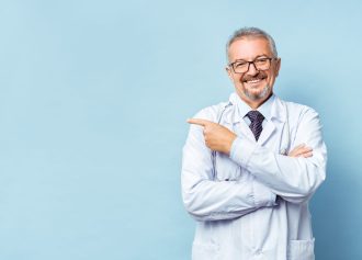 Cheerful mature doctor posing and smiling at camera, healthcare and medicine. Isolate on blue background