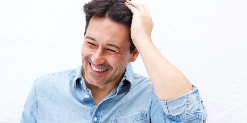 Close up portrait of mature guy smiling with hand on head against white background