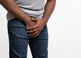 Cropped of black man holding his groin over white background, copy space
